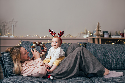 Step into a world of festive whimsy as this mom and her baby share playful moments on the living room sofa, with baby being adorned with adorable antlers.