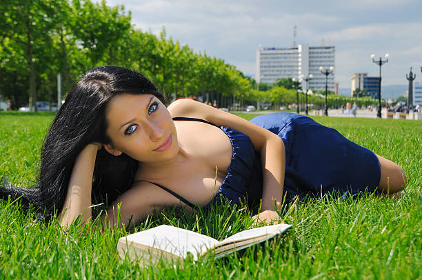 Cheerfull  young woman  holding  open book and reading on bench in autumn park