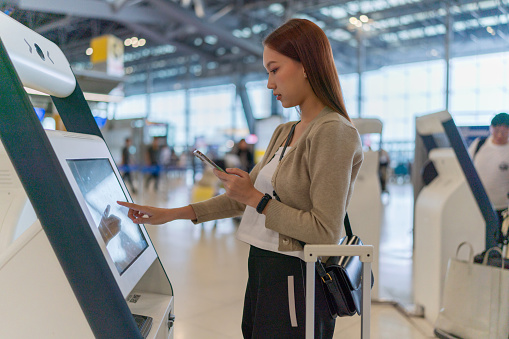 Young Asian Woman checking in at the airport using an automated self service check-in kiosk. Ready to travel. Business trip. Business travel. Travel and vacation concept