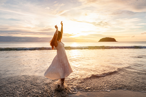 Young woman traveler dancing and enjoying beautiful Sunset on the tranquil beach, Travel on summer vacation concept