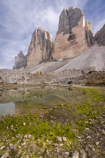 Massive rock formation of Tre Cime reflecting in small pond, vertical shot, Dolomites, Italy