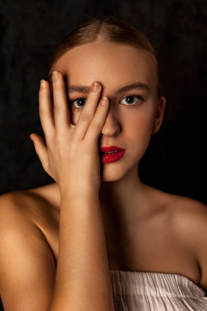 modèle d’adolescente parfait visage couvert avec la main dans l’ombre sur fond noir, œil regardant la caméra. une adolescente dans l’image de poupée porte du blanc, sombre prise de vue en studio. concept de soins de beauté pour le corps. copier  - mannequin naked female doll photos et images de collection