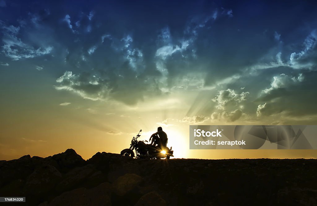 Freedom and loneliness A man is sitting on a motorcycle and watching the setting sun under a gold-blue sky Motorcycle Stock Photo