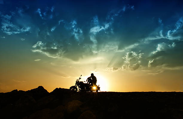Freedom and loneliness A man is sitting on a motorcycle and watching the setting sun under a gold-blue sky motorcycle photos stock pictures, royalty-free photos & images
