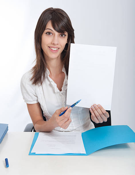 Happy business woman with your message ..Young woman at a desk pointing with her pen to a blank paper. Ideal for inserting your own message. read the fine print stock pictures, royalty-free photos & images