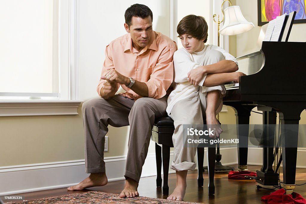 Serious father talking to teenage son at home Serious father talking to teenage son at home by piano Discussion Stock Photo