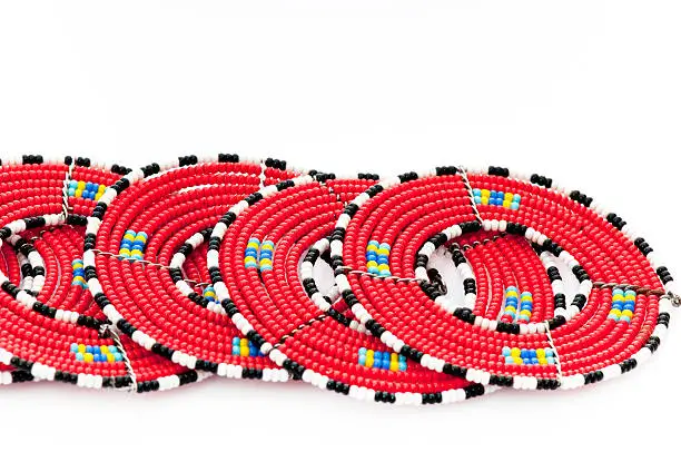 "Collection of Masai beaded mats or body ornaments in red with a blue and yellow decoration, ringed in black and white. On white."