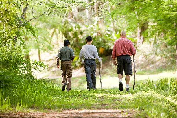 Hispanic father and sons hiking on trail in woods