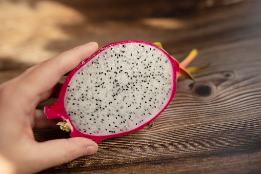 Close up male hand holding dragon fruit on wooden background.