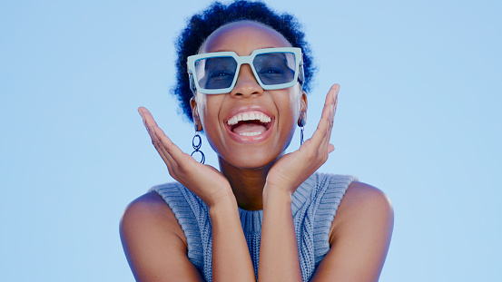 Black woman, sunglasses and face in studio with happy, excited and fashion creativity by blue background. Gen z girl, glasses or shades for vision, portrait and happiness for accessory by backdrop