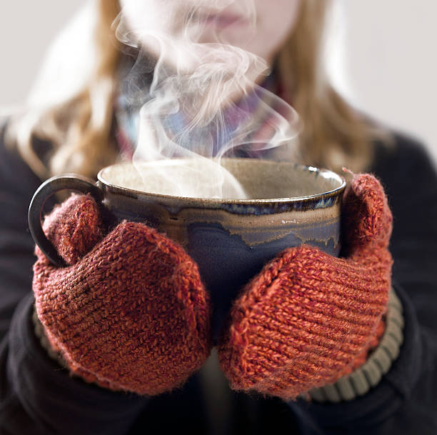 detail of a woman with woolen gloves holding a hot steaming cup