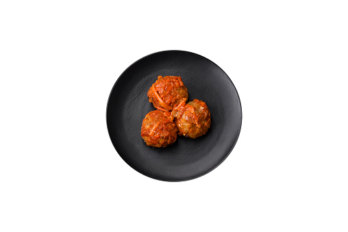Delicious fresh meatballs from minced meat or fish with tomato sauce, carrots, onions, salt and spices on a dark concrete background