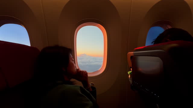 woman flying in an airplane, looking out the window at sunset time