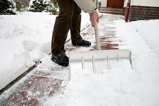 Photo of Man shoveling snow at a footpath