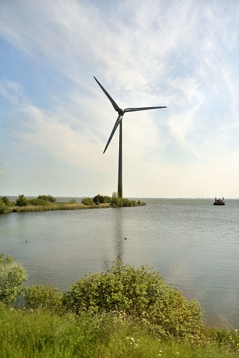 A sailboat next to a wind turbine in a tranquil lake