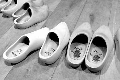 A line of traditional Dutch wooden clogs arranged on the floor, in grayscale