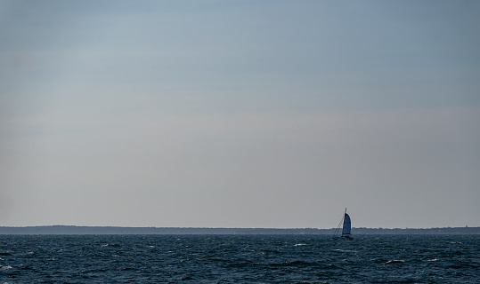 Solitary yacht on Nantucket Sound.  It is on the horizon with a morning sky behind it.