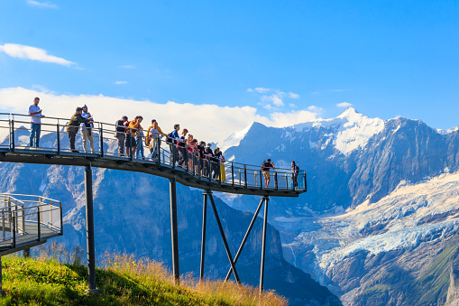 Grindelwald,  Switzerland - August 6, 2022: Tourists take photos on the First Cliff Walk, a popular viewing platform on the First mountain in Grindelwald, which offers with stunning Alpine views