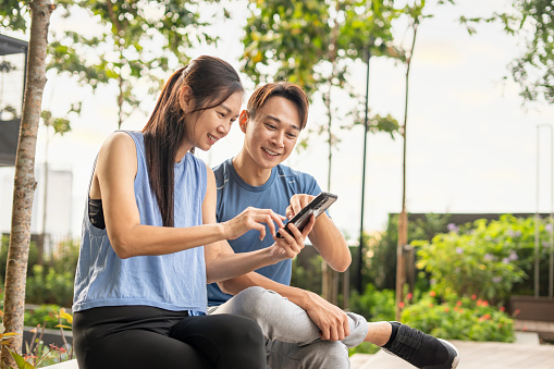 Athlete friends sitting outdoor in casual clothing using smart phone