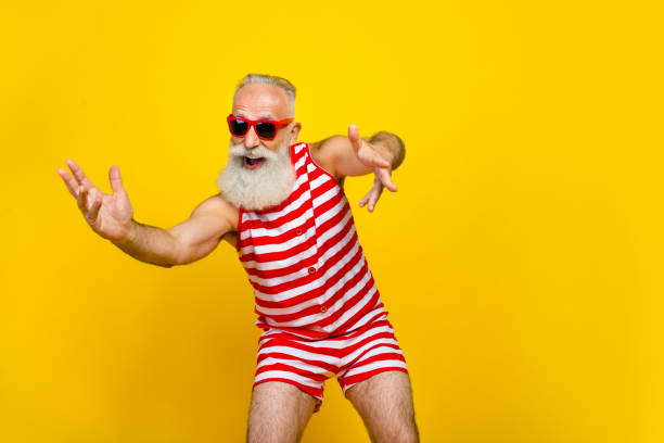 istock Photo of funky cheerful elderly guy dressed striped red swimsuit dancing empty space isolated yellow color background 1768454086