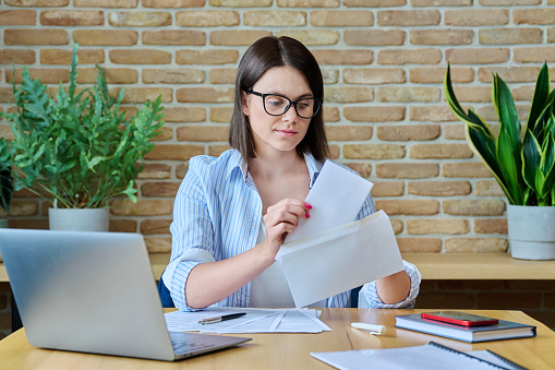 Young business woman with paper letter sitting at desk with computer in office. Business, bank chat payments, contracts, agreements, business people concept