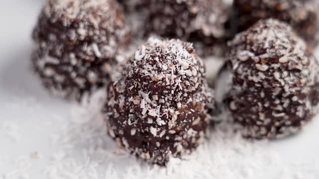Homemade chocolate truffles with falling coconut shavings. Cooking healthy treats. Rotation. Slow motion