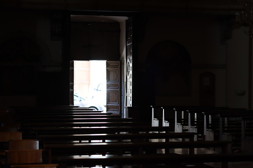 View across empty wooden pews in a quiet church towards an open doorway