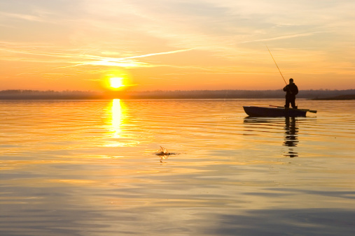 Fisherman on fishing boat in river at sunset