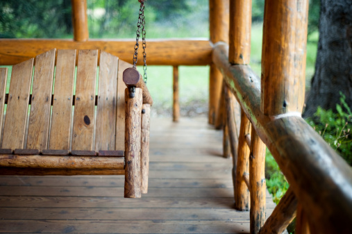 The front porch swing of a rustic log cabin.