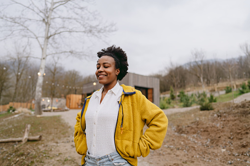 Photo of a smiling African American woman, during a prolonged weekend in front of a cabin house - her rental home for the weekend