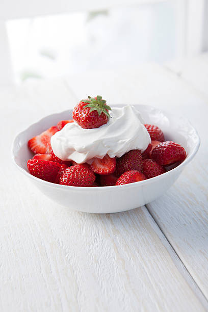 White bowl of strawberries with whipped cream on top stock photo