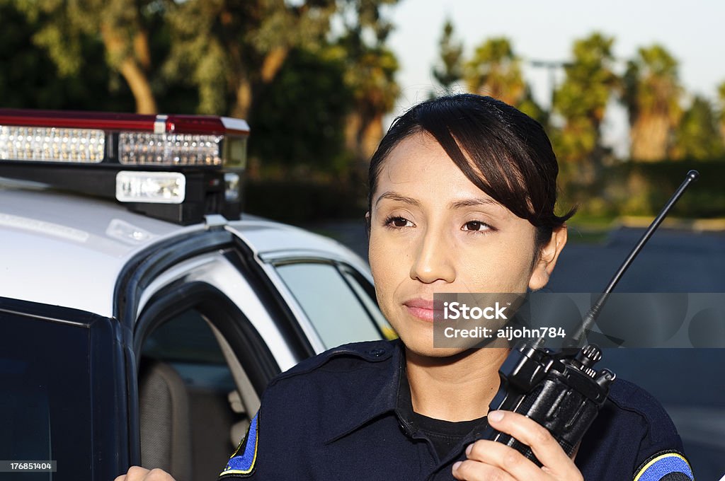police officer a Hispanic female police officer stands next to her patrol car while holding her radio. Police Force Stock Photo