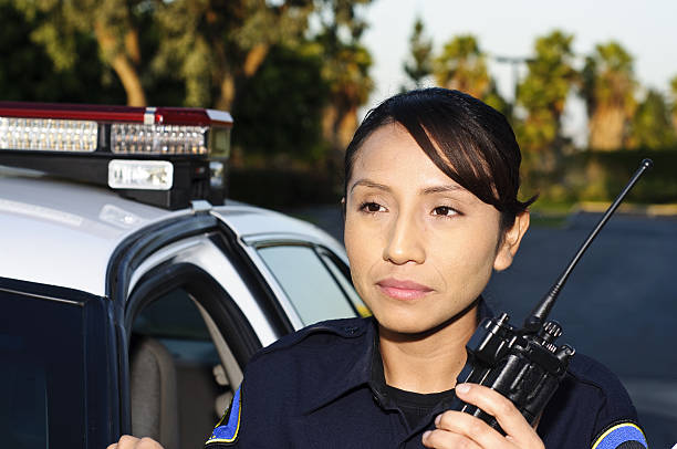 police officer a Hispanic female police officer stands next to her patrol car while holding her radio. female police officer stock pictures, royalty-free photos & images