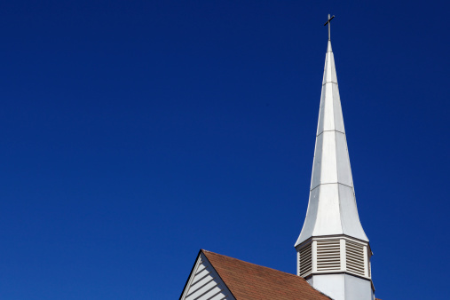 Thin pointy metal church steepl against a dark blue sky