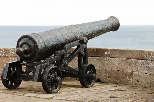 An old canon faces out to sea on a battlement wall in an English castle.