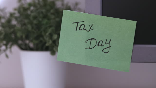 A green paper notes with the reminder Tax Day on it sticked on to a monitor at an office workplace.