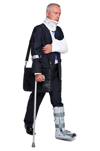 Injred businessman walking with a crutch isolated on white "Photo of a badly injured businessman walking on cructhes carrying a briefcase, isolated on a white background." man with arm sling stock pictures, royalty-free photos & images