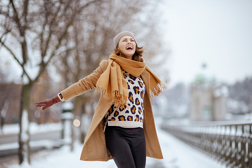 Full body of positive young female in cozy clothes and stylish sunglasses, stretching arms in side plank yoga pose with open legs on snowy ground against blue sky