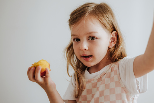 Young girl looking at camera while having fresh fruit for a snack at home.