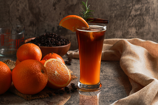 Iced Americano black coffee with lower layer orange juice in the glass. Rosemary with cinnamon on top. citrus fruits and coffee beans background. Coffee and orange juice concept.