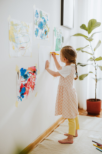 Unrecognizable young girl painting with a felt tip pens on a paper hanging on a nursery wall.