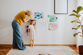 Mother Measuring Daughter's Height And Marking It On A Living Room Wall