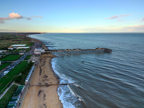 High angle drone view over the beach and pier in the coastal town of Southwold in Suffolk, UK. On the beach people are playing on the sand.