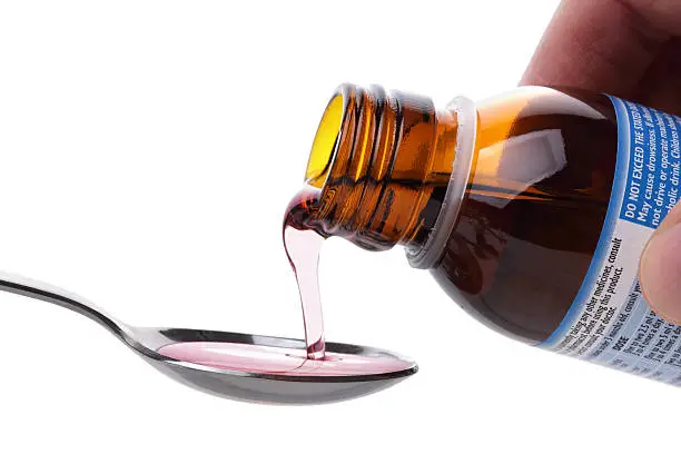 Pouring cough medicine onto a spoon from a bottle