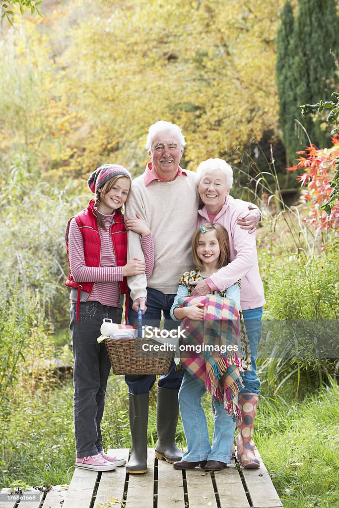 Grandparents With Grandchildren Carrying Picnic Basket By Autumn Grandparents With Grandchildren Carrying Picnic Basket By Autumn Woodland Smiling At Camera Autumn Stock Photo