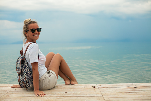 Female sitting on pier over water. Cheerful young woman on wooden pier above tropical reef sea.