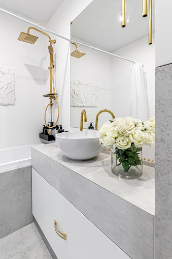 A modern bathroom in light colours with gold fixtures and a bouquet of white flowers.
