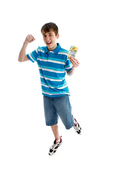 A teenage boy leaps for joy and makes a fist of success.  He is holding some money in the other hand.  White background.