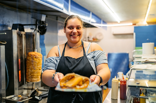 Portrait of a female food service worker serving a plate with fried cheese in a diner.