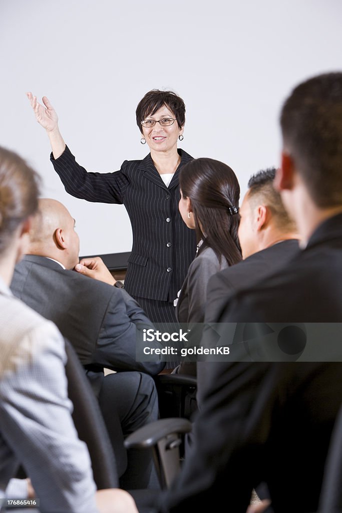 Hispanic woman speaking to group of businesspeople "Hispanic woman standing in front, speaking to group of business people" Education Training Class Stock Photo